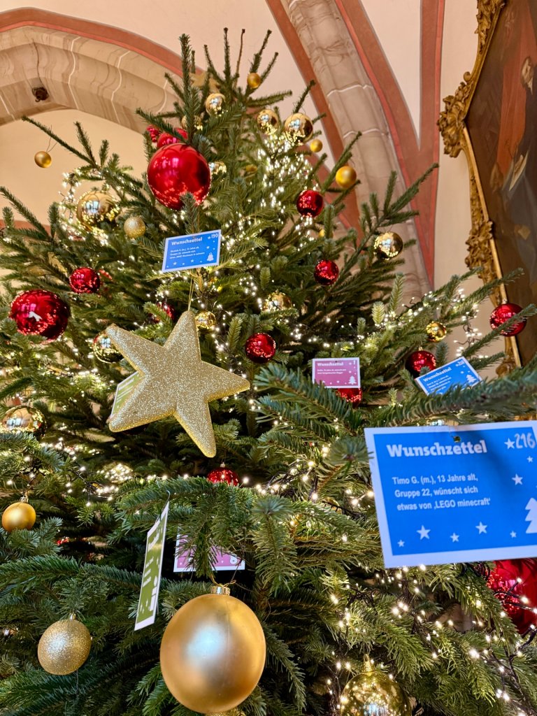 Vue d'en bas sur l'arbre à listes de souhaits rouge et or de l'hôtel de ville d'Aix-la-Chapelle ainsi que sur une carte de vœux bleue accrochée dessus.