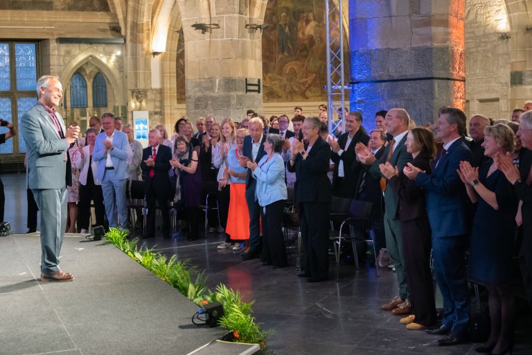 Le public de la salle du couronnement de l'hôtel de ville d'Aix-la-Chapelle est debout et applaudit le lauréat du prix d'ingénierie d'Aix-la-Chapelle, qui se tient sur une scène.
