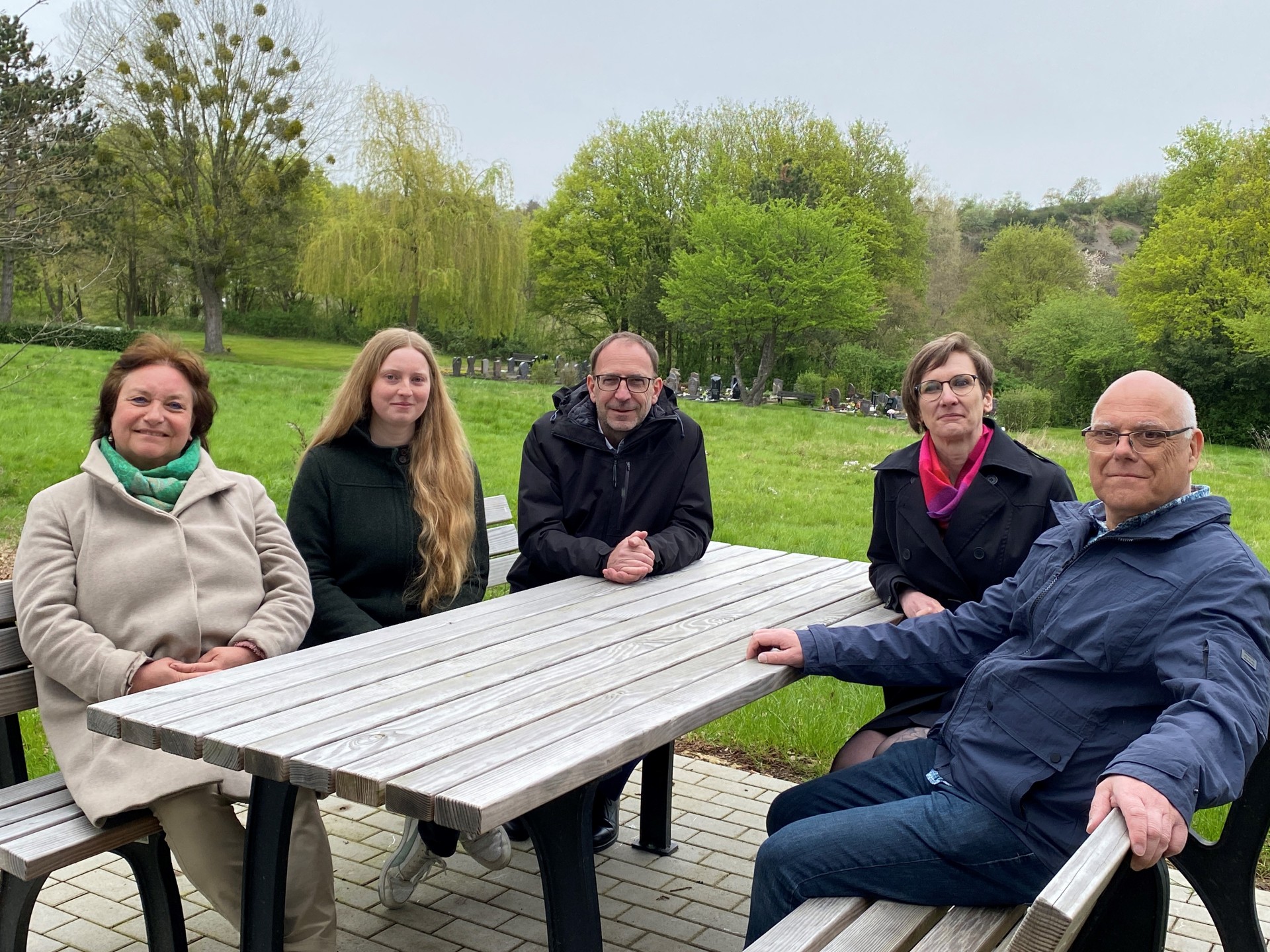 Cinq personnes sont assises à une table qui se trouve sur une pelouse du cimetière d'Eilendorf.