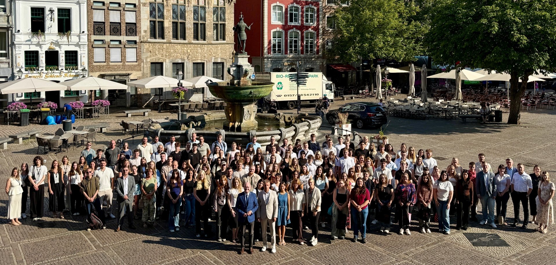 Bienvenue à Aix-la-Chapelle Un groupe de personnes se tient devant la fontaine de Charles et attend avec impatience le début de la formation.