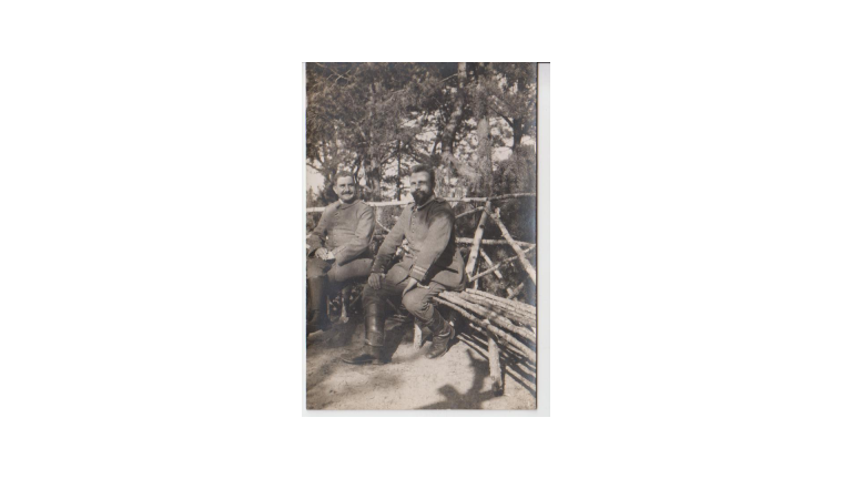 Une reproduction d'une photo datant de 1901. Deux hommes en uniforme sont assis sur un banc.
