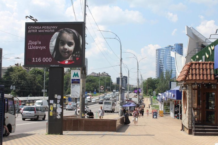 Un grand panneau d'affichage avec la photo d'un enfant et un numéro de téléphone, situé sur une rue principale d'une ville.