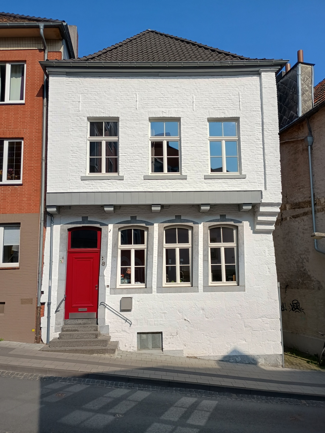 Un bâtiment résidentiel historique avec une façade blanche et une porte d'entrée rouge distinctive se trouve dans la rue principale de Burtscheid.