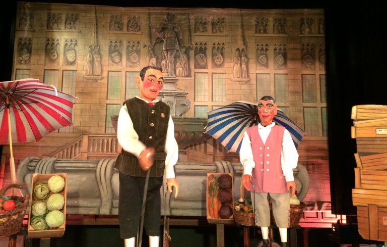 Deux marionnettes à tringle se tiennent devant un décor peint de l'hôtel de ville d'Aix-la-Chapelle.