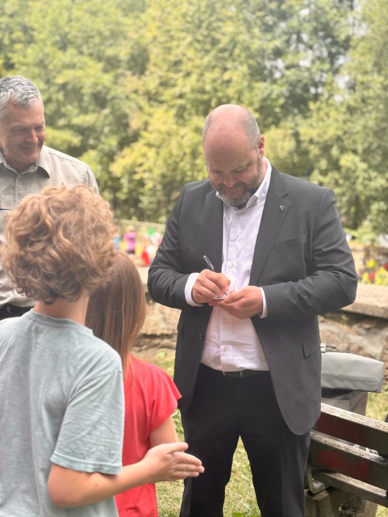 Plusieurs enfants font la queue. À l'arrière-plan, on voit le maire Ziemons en train de signer un autographe.