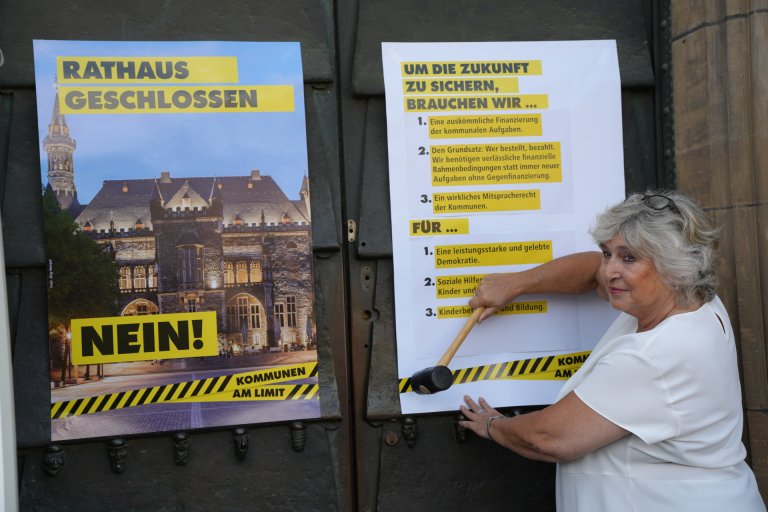 Une femme, un marteau à la main, se tient devant la porte de la mairie d'Aix-la-Chapelle et accroche une affiche.