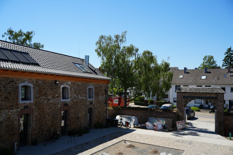 Vue sur la cour intérieure d'un domaine rénové. Centre de la photo, derrière : Arc de l'entrée. A gauche, le manoir.