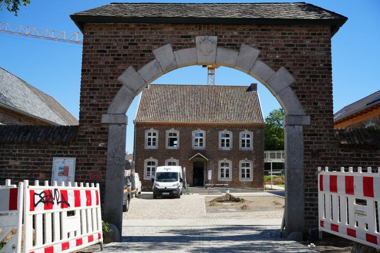 Arc de porte d'un domaine, en arrière-plan une étable rénovée.