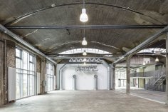 De piazza is te zien vanaf de achterkant, kijkend in de richting van de ventilatiekanalen. Er zijn grote ramen van vloer tot plafond aan de linkerkant en rechts is een trap te zien.