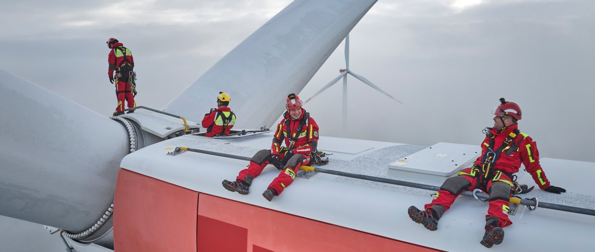 4 geüniformeerde hoogteredders zitten gezekerd op een ongeveer 150 meter hoge gondel van een windturbine.