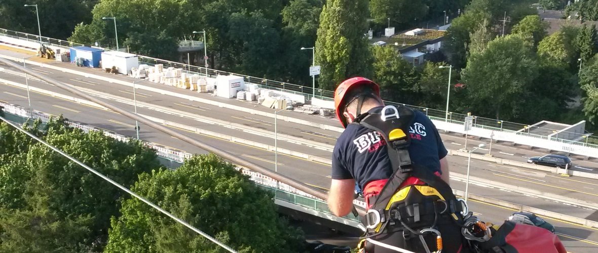 Een geüniformeerde officier van het hoogtereddingsteam van de beroepsbrandweer van Aken zit op een ongeveer 40 meter hoge pyloon van de Keulse Rijnkabelbaan.