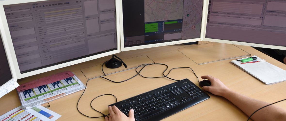 Elke werkplek in het controlecentrum bestaat uit minstens 4 beeldschermen, waarop veel programma's tegelijk open staan, en een headset met microfoon. Een medewerker zit aan zijn bureau en typt iets op zijn toetsenbord.
