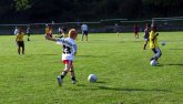 Een oefening op het voetbalveld. Een coach begeleidt de kinderen, die elk met hun eigen bal spelen.