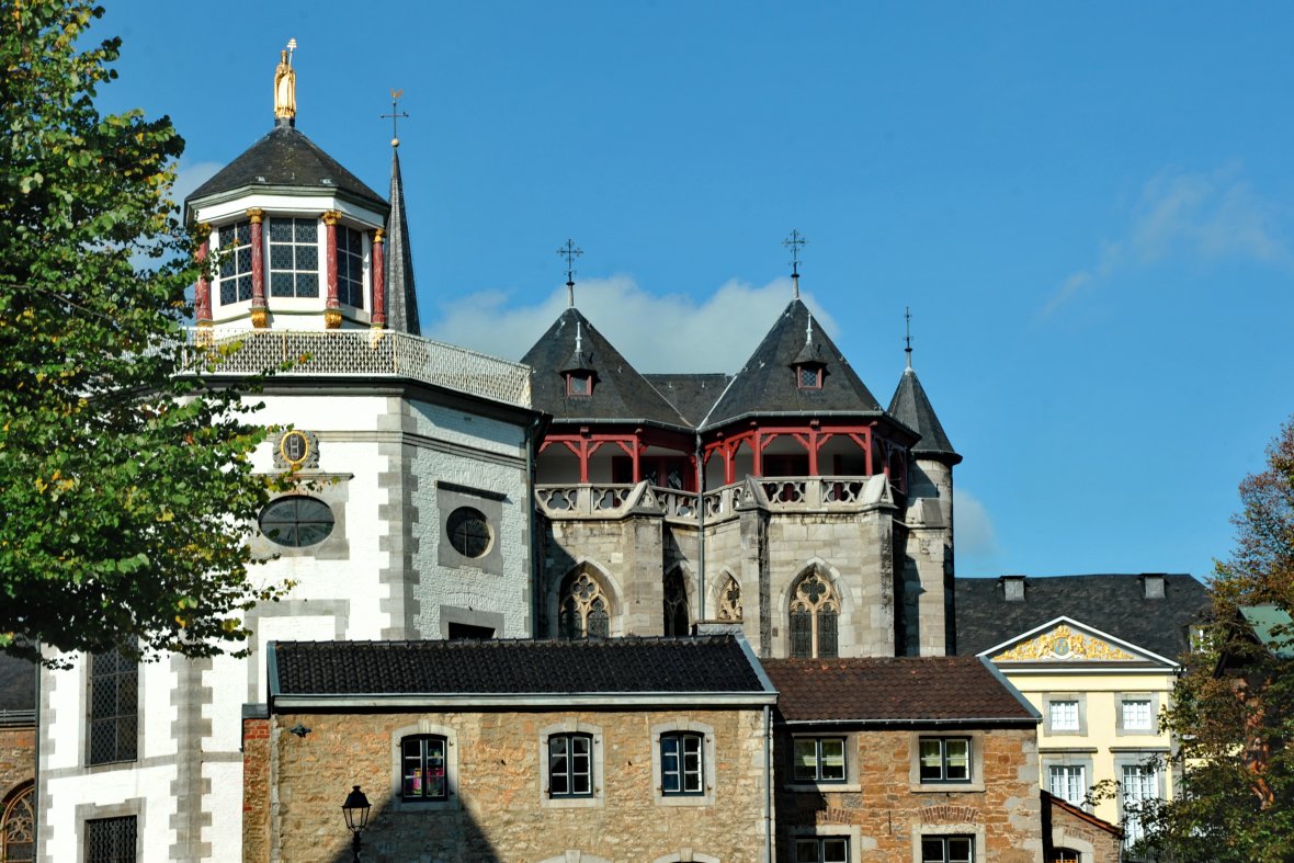 St Kornelius Kornelimünster De St Korneliuskerk onder een blauwe hemel en zonneschijn. Een groene loofboom torent uit in de linkerrand van de foto.