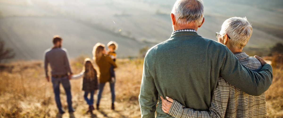 Achteraanzicht van omarmde grootouders die naar hun familie kijken in een veld op een herfstdag.