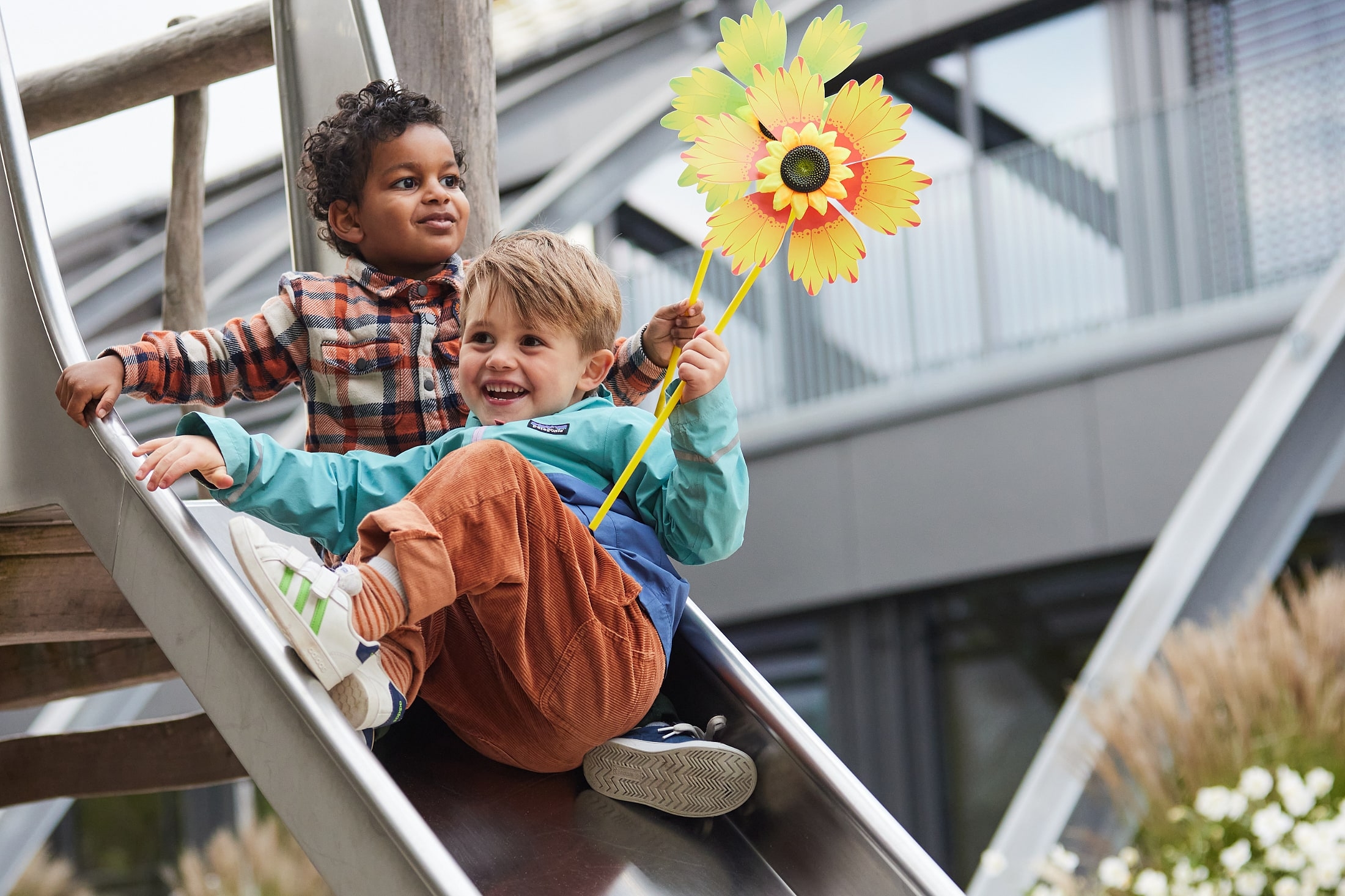 Twee kinderen op een glijbaan. Eén kind houdt een pinwiel vast