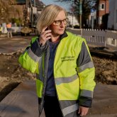 Claudia met een neongeel hesje van de toezichthouder NRw staat op straat aan de telefoon.