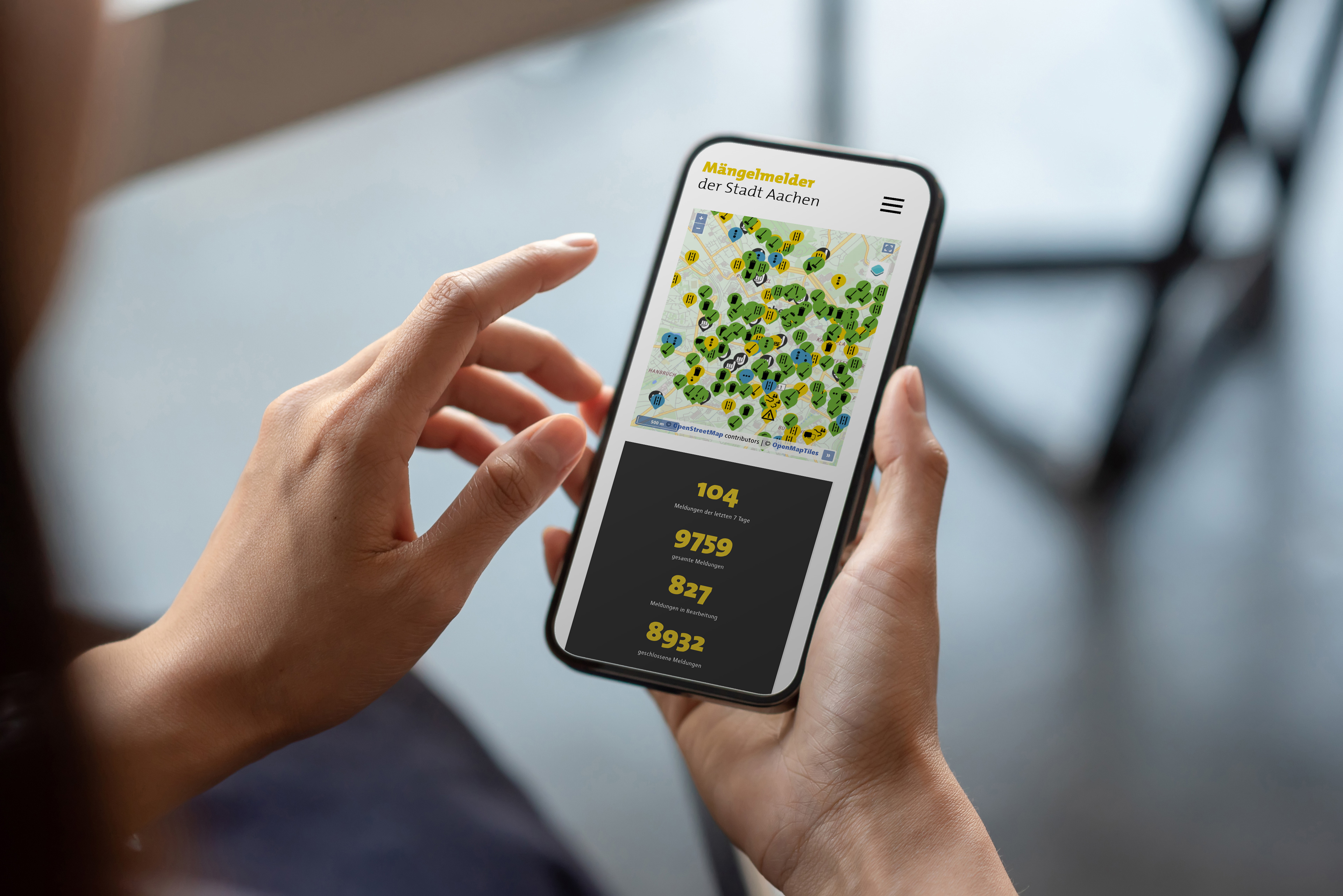 Een persoon heeft een smartphone in de hand en heeft het defectenrapport van de stad Aken geopend.