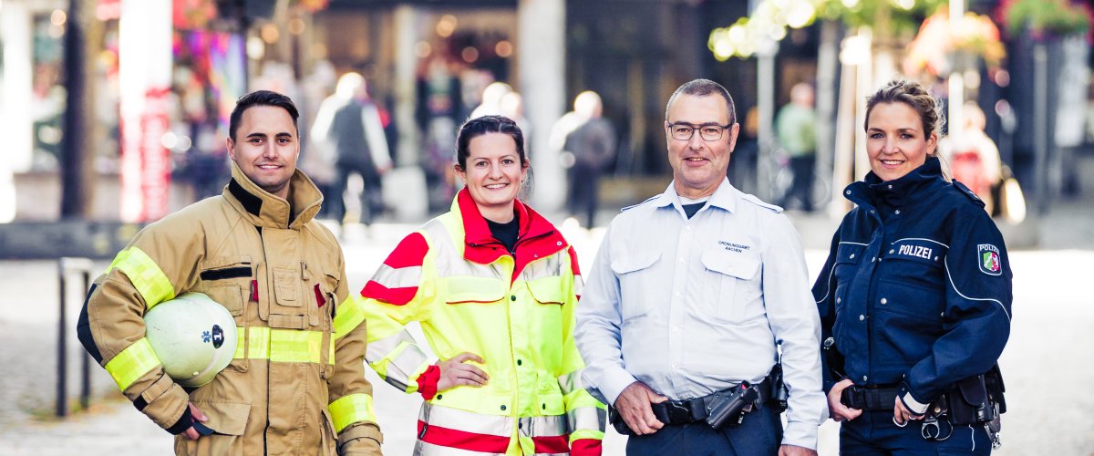 4 mensen staan voor de camera op Katschhof: een brandweerman, een paramedicus, een officier van de OSD en een politieagente.