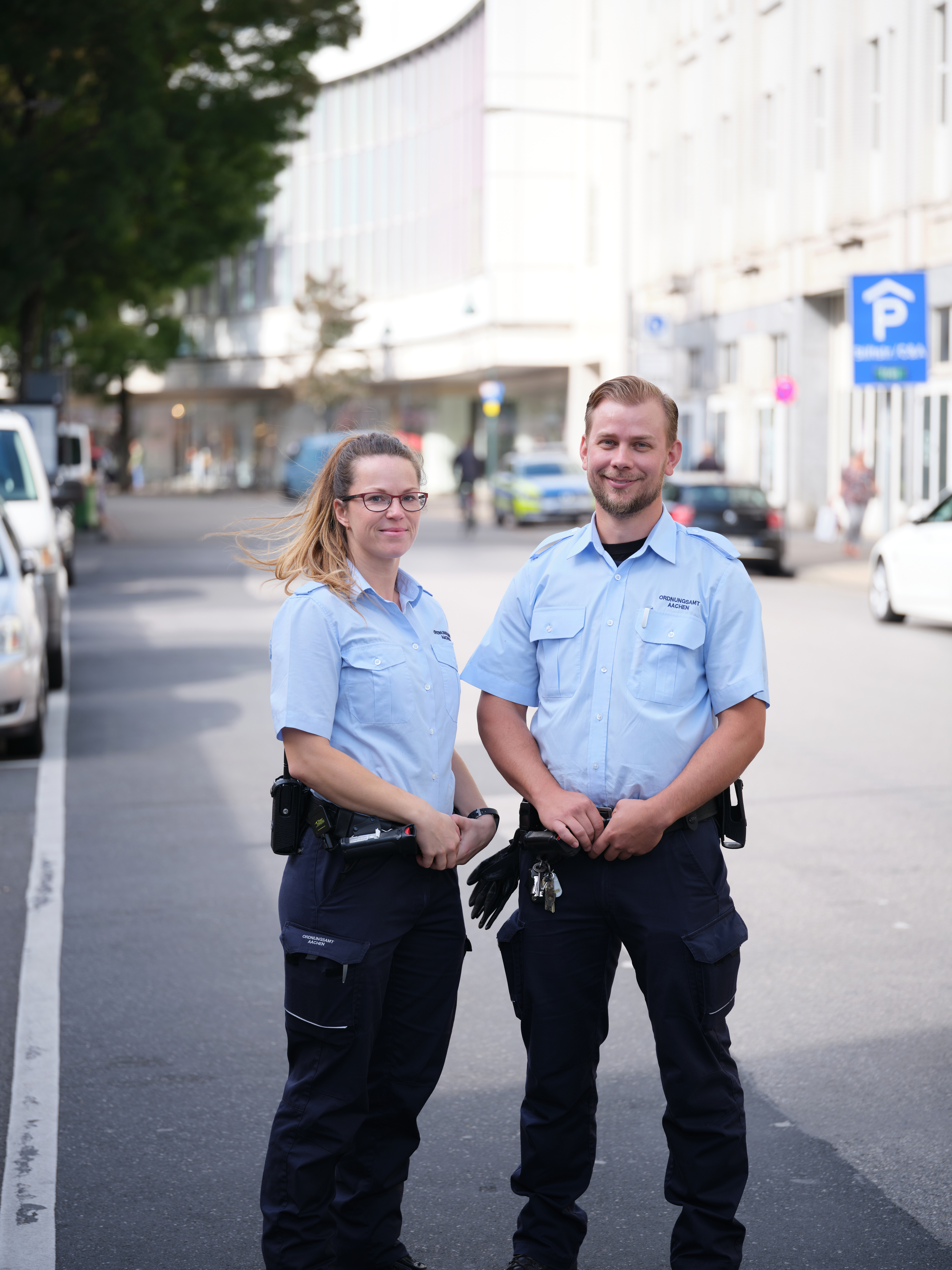 Twee agenten van het openbare orde bureau staan op straat en kijken vriendelijk in de camera.