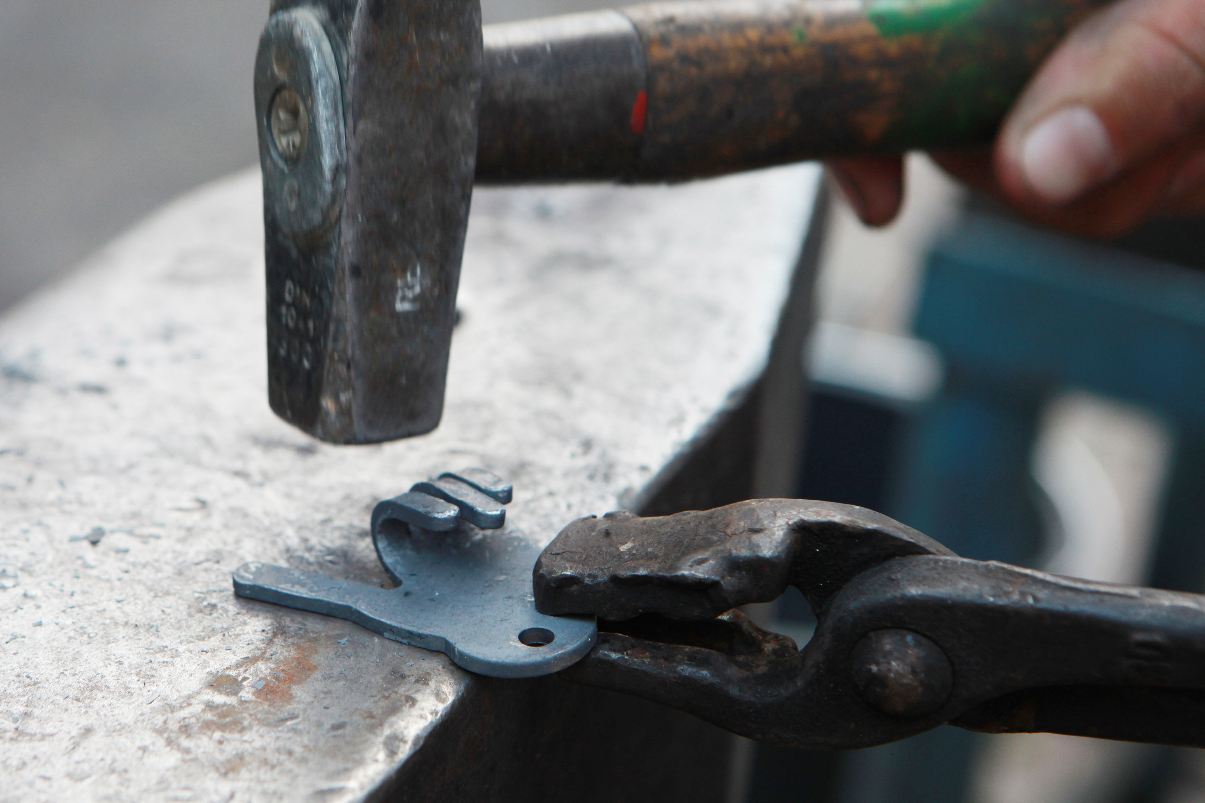 Close-up: Een kleine metalen plaat in de vorm van het stadhuis van Aken wordt bewerkt op een aambeeld door de hamer van een smid.