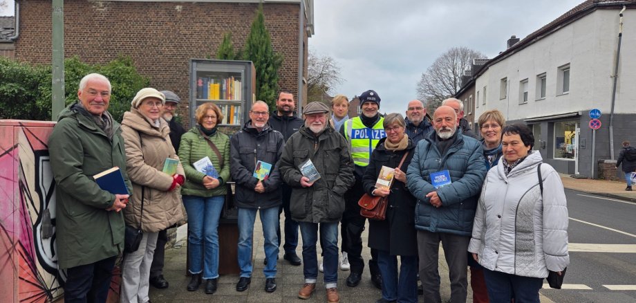 Een groep mensen met boeken in hun handen staat naast een boekenkast op een stoep.