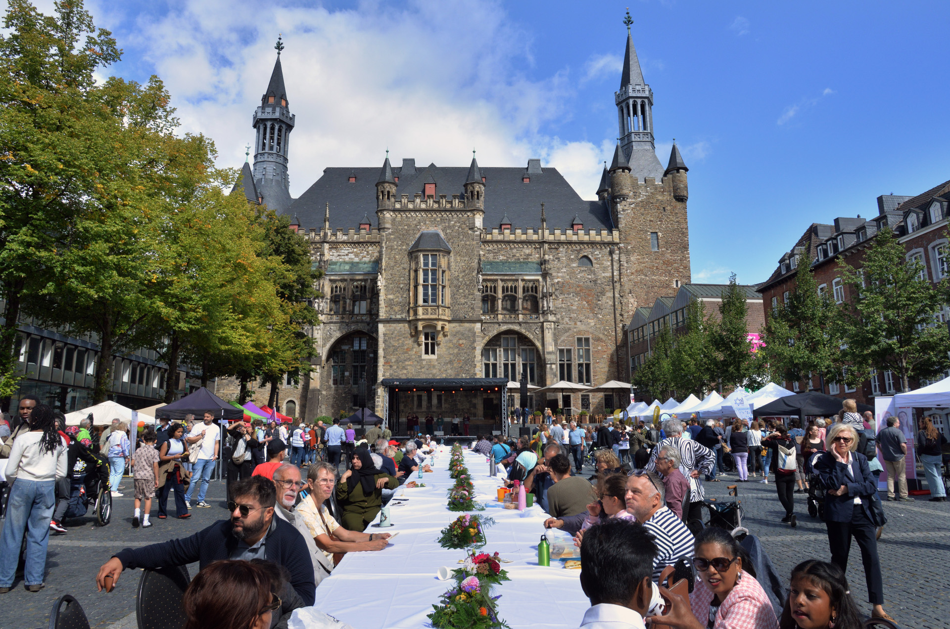 Een lange tafel van 30 meter op een plein, omringd door mensen, met het stadhuis van Aken op de achtergrond