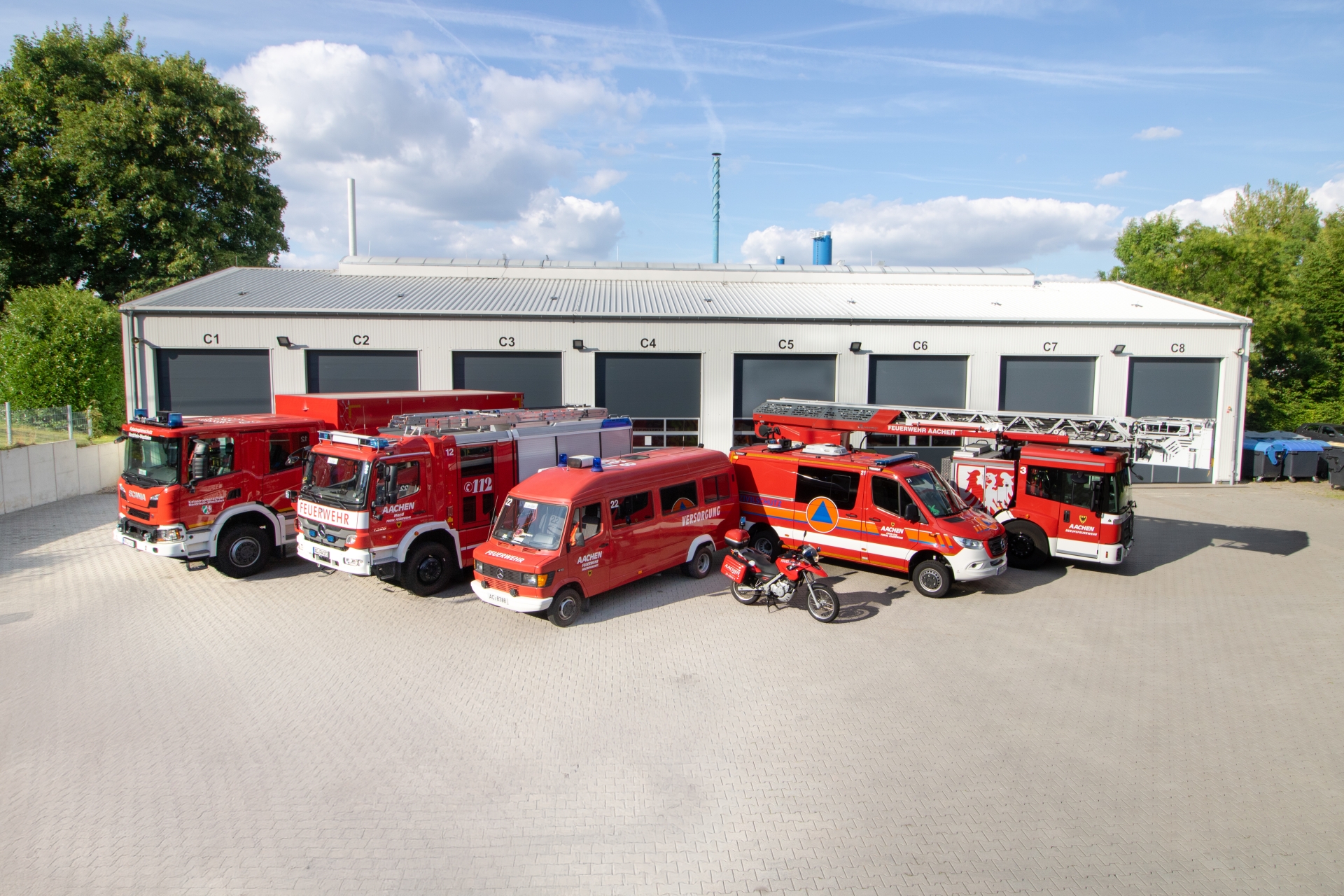 Vijf rode brandweerauto's en een motor staan geparkeerd voor een voertuigenhal.