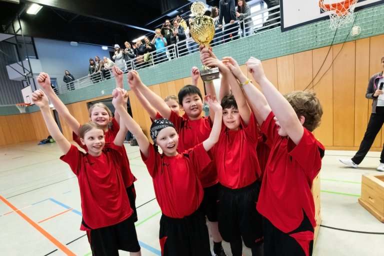 Kinderen in rode truitjes houden een zilveren trofee omhoog