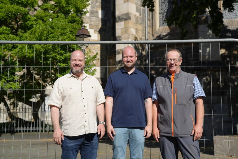 Drie mannen staan voor een bouwhek.