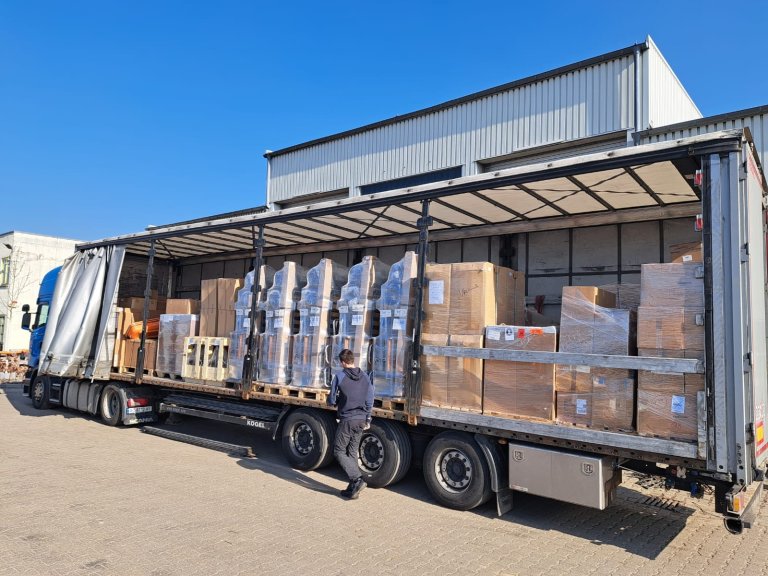 Een vrachtwagen met open zijpanelen, volledig geladen met noodgoederen.