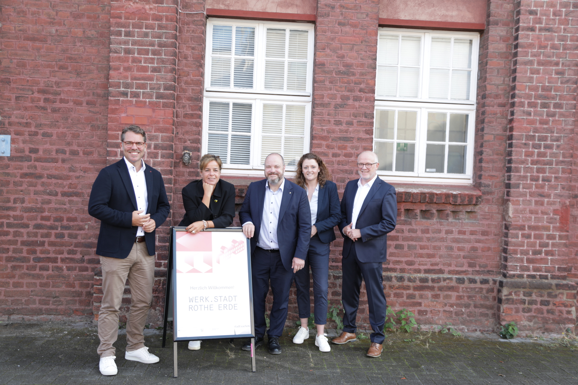 Vijf mensen – drie mannen en twee vrouwen – staan voor een muur: Thomas Hissel, wethouder van Economische Zaken, Mona Neubaur, minister van Economische Zaken van Noordrijn-Westfalen, Dr. Michael Ziemons, burgemeester van Aken, Judith Abels, projectleidster, en Dieter M. Begaß, hoofd van de dienst Economische Ontwikkeling. 
