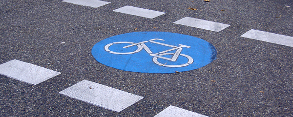 Großes blaues Radwegsymbol auf Straßenpflaster, flankiert von unterbrochenen weißen Linien