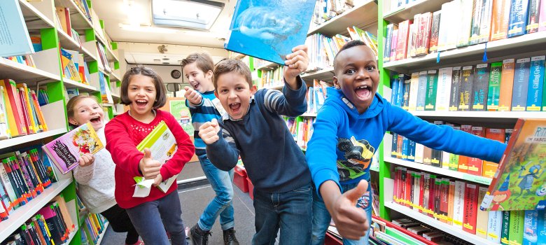 Mehrere Kinder im Bücherbus die lachend Bücher in den Händen halten