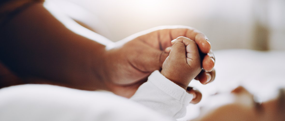 Kleine Babyhände die die Hände eines Elternteils halten.