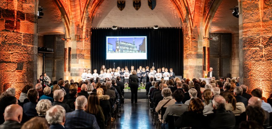 Neujahrsempfang 2026 Bestuhlter Krönungssaal gefüllt mit Gästen und auf der Bühne ein Kinderchor und Dirigent.