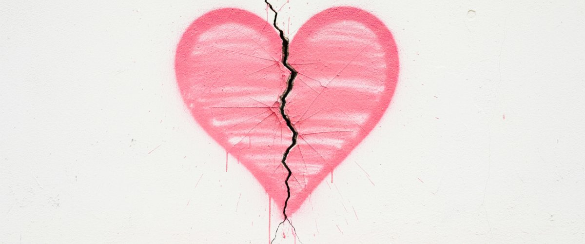 Pink broken heart shape graffiti split by wall crack symbolising heartbreak and emotional separation, romantic relationships, divorce