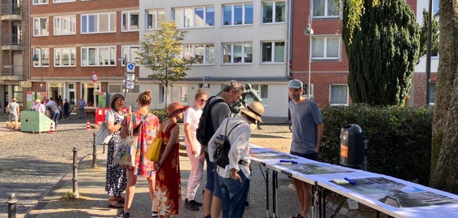 Teilnehmende einer Bürgerbeteiligung informieren sich vor Ort über die Neugestaltung der Klappergasse und Rennbahn in Aachen anhand eines Renderings