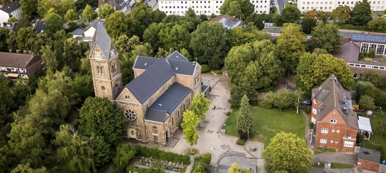 Luftansicht der Kirche St. Katharina in Aachen Forst. Mit vielen Bäumen in der Umgebung und ein Kirchenvorplatz