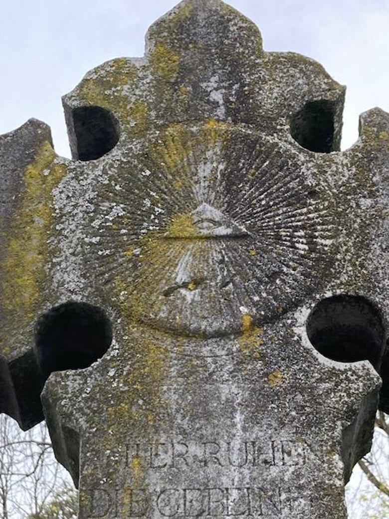 Detailansicht eines Grabkreuzes im Fokus auf das "Gottesauge"