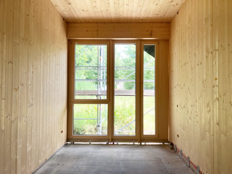 Die Holz-Alu-Fenster wurden montiert, zu erkennen sind die innenliegenden Holzoberflächen und der Öffnungsflügel.