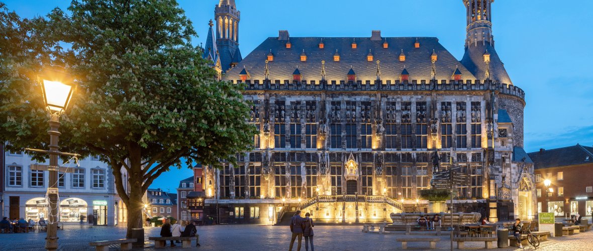 Rathaus, Aachen Das beleuchtete Aachener Rathaus vom Marktplatz aus in der Abenddämmerung. Im Vordergrund sind ein Baum und der Karlsbrunnen zu sehen und Laternen leuchten.