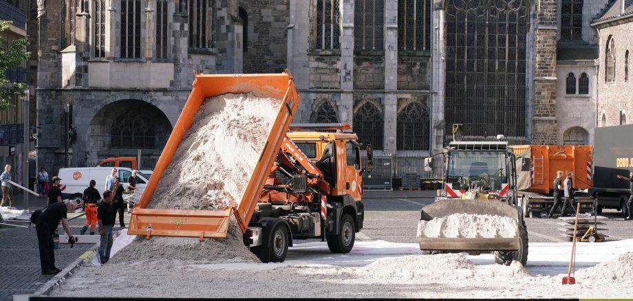 Bagger und Lastwagen verteilen bergeweise Sand in einem riesigen Sandkasten auf dem Aachener Katschhof. Im Hintergrund der Aachener Dom und blauer Himmel.