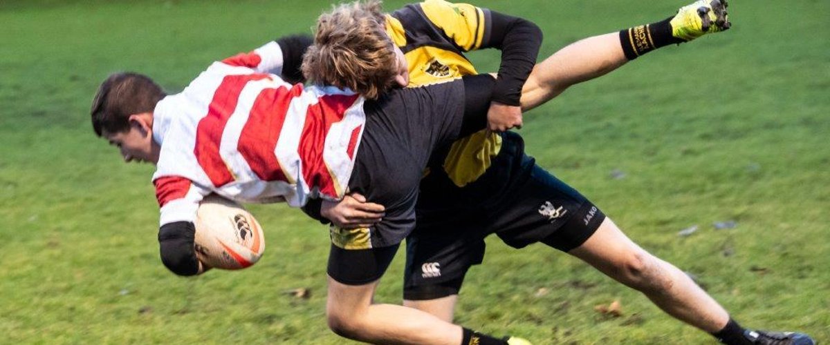 Zwei Rugby Spieler kämpfen um den Rugbyball. Dabei versucht ein Spieler den anderen umzuwerfen