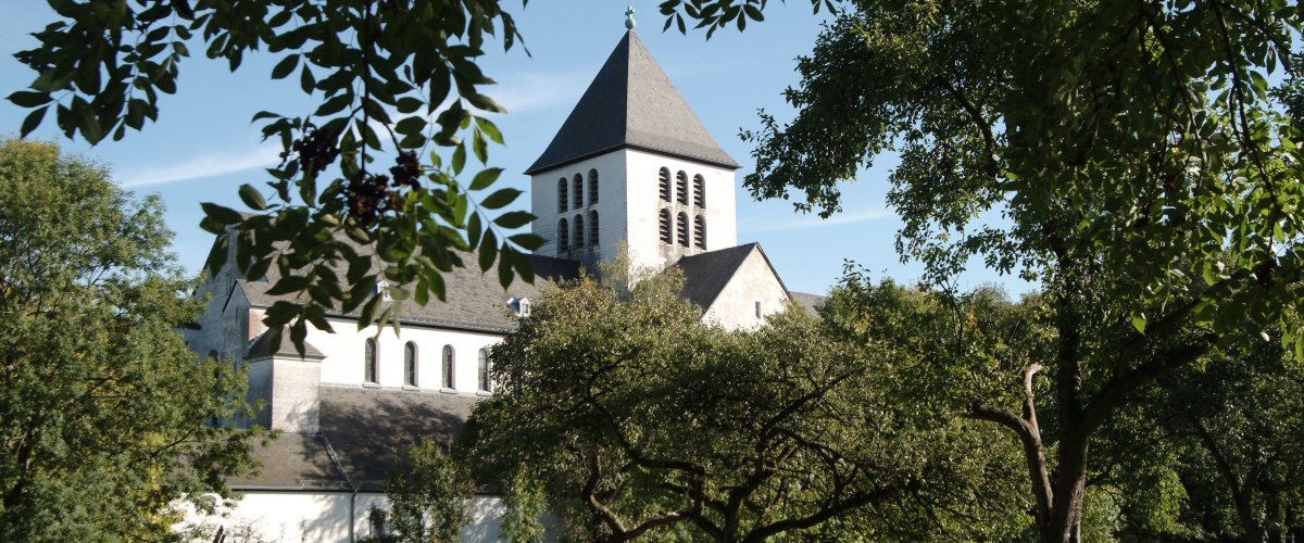 Benediktinerkloster Kornelimünster Das weiße Benediktinerkloster bei Sonnenschein. Im Vordergrund liegt eine Obstwiese.