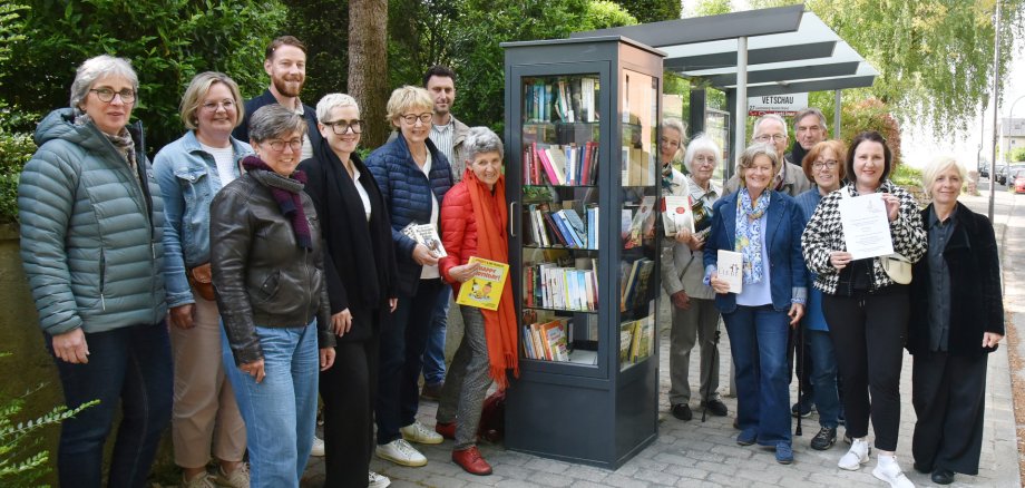Eine Gruppe von Menschen steht neben einem Glasschrank mit Büchern.