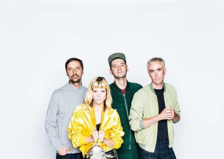 Die Band MIA. steht vor weißer Wand und schaut in die Kamera. Sie besteht aus drei Männern und einer Frau.