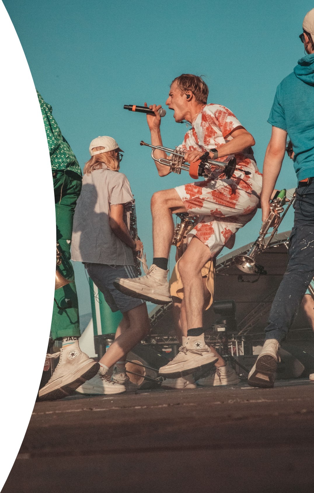 Ein Mitglied der Band Knallblech singt leidenschaftlich in ein Mikrofon. Sie stehen auf einer Freiluftbühne und der Himmel ist blau.