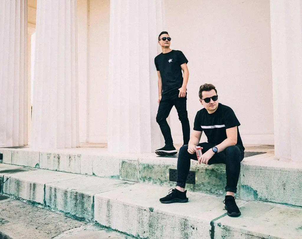 Die beiden DJs Harris und Ford posieren ganz in schwarz gekleidet an einem hellen Haus mit großen Säulen.