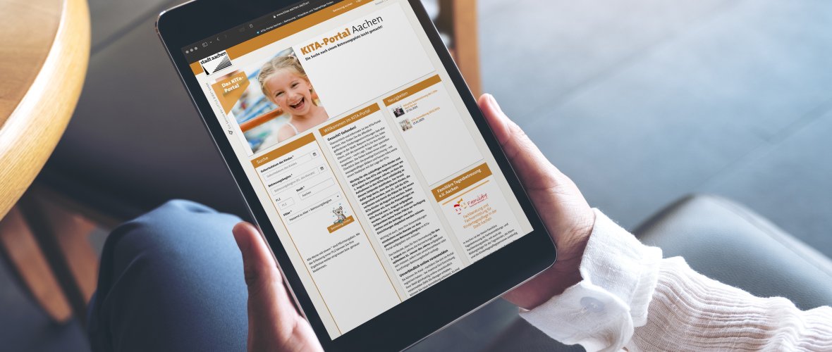 Draufsicht einer Frau im Schneidersitz hält ein Tablet mit dem geöffneten Kita-Portal.